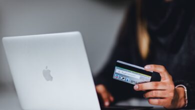 A person sitting in front of a silver Macbook laptop and holding a credit card.
